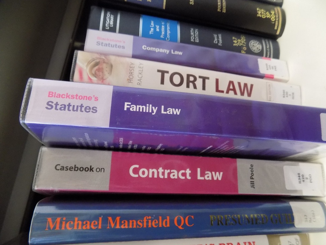 En stak juridiske lærebøger på en hylde, med en fremtrædende bog med titlen 'Family Law' fra Blackstone's Statutes-serien. Andre synlige juridiske tekster inkluderer Tort Law, Contract Law og Company Law, der repræsenterer de juridiske ressourcer, der bruges i familieretssager.