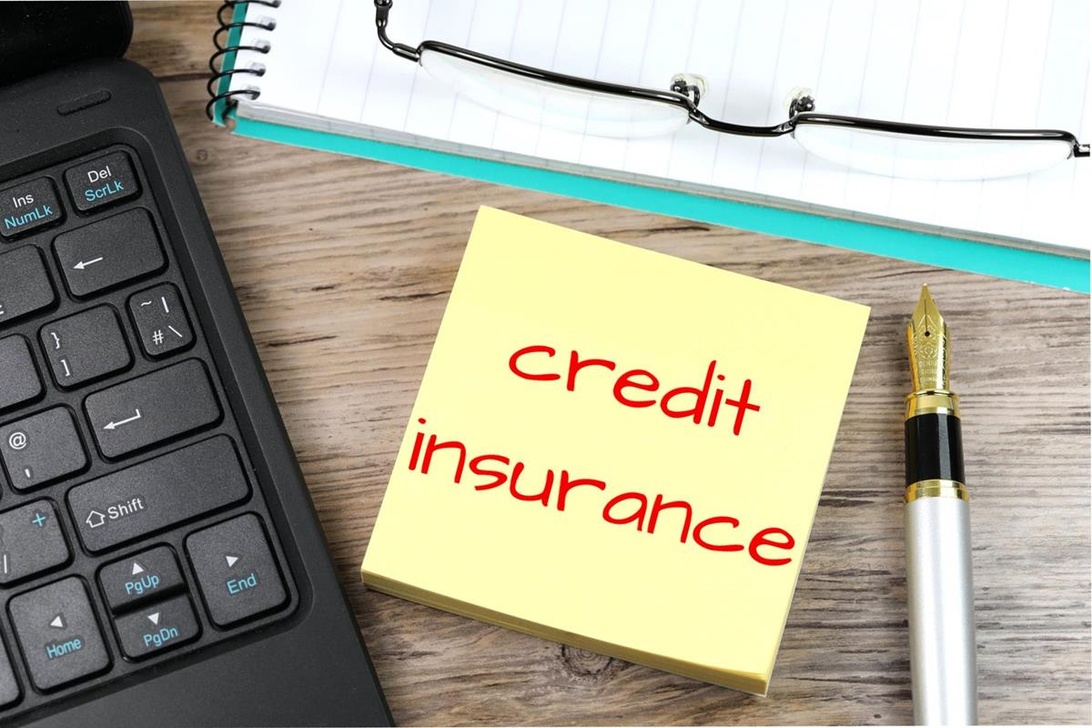 En gul sticky note med 'credit insurance' skrevet med rød tekst på et skrivebord ved siden af en bærbar computer, hvilket illustrerer vigtigheden af at huske detaljerne i forretningsaftaler.