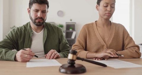 Par underskriver dokumenter ved et bord med en dommerhammer i forgrunden